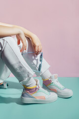 Close up female legs in white jeans and retro style high-top multicolor sport sneakers shoes...