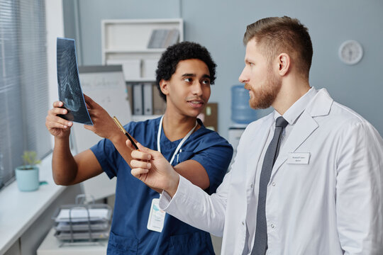 Waist up portrait of two doctors holding brain X-ray image and discussing patient case in medical clinic, copy space