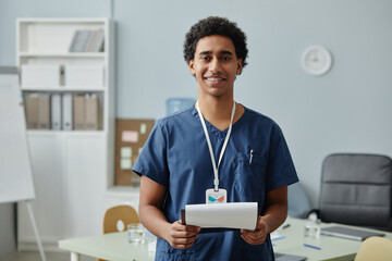 Waist up portrait of young Arabian man wearing scrubs uniform and holding clipboard in clinic, copy...