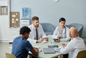 Diverse group of doctors in discussion at meeting table in clinic interior, copy space