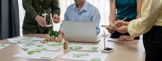 Cropped image of skilled businessman presented eco-friendly house project to general manager at meeting table with wooden block, windmill model and environmental document scatter around. Delineation. - obrazy, fototapety, plakaty