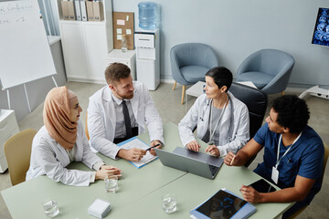 High angle view at multiethnic group of doctors at meeting table discussing work issues in clinic, copy space