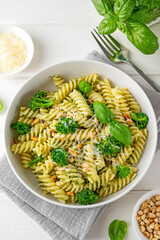Vegetarian pasta with pesto sauce, broccoli, parmesan cheese and pine nuts on a white wooden background. Healthy food.