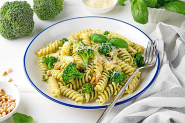 Vegetarian pasta with pesto sauce, broccoli, parmesan cheese and pine nuts on a white wooden...