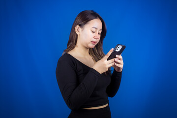 A young Asian woman is happy and smiling while using a smartphone on a blue background