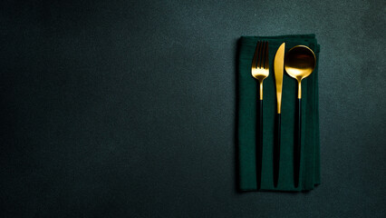 Cutlery: fork, knife and spoon on a green napkin. Free copy space. Top view On a dark background.