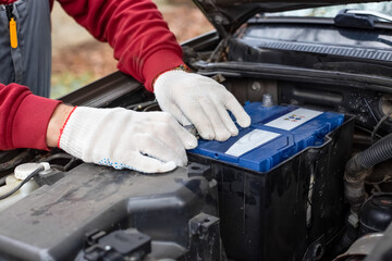 auto mechanic installs a car battery under the hood of a car. Car maintenance and repair.