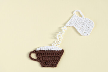 Milk is poured into a cup. A cup of coffee and a jug of milk. All elements are crocheted.