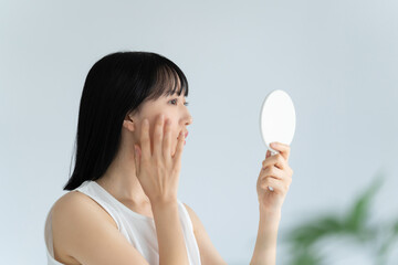 鏡で肌をチェックする白い服の若い女性