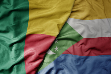 big waving national colorful flag of benin and national flag of comoros .