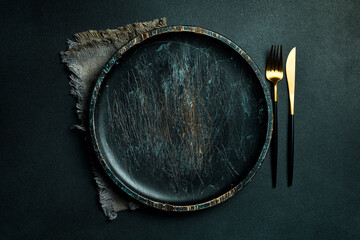 Gold knives and forks on a black background, empty black plate. Beautiful gold cutlery. View from...