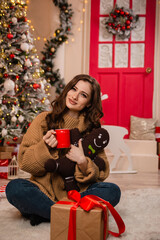 Beautiful young woman with a red mug of coffee in her hands against the background of a Christmas tree.
