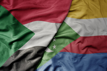 big waving national colorful flag of sudan and national flag of comoros .