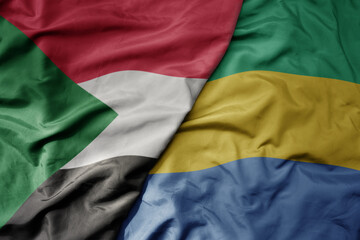 big waving national colorful flag of sudan and national flag of gabon .