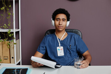 Front view portrait of young Middle Eastern man as male doctor sitting at desk in office and...