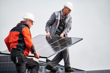 Technicians installing solar panel system on roof of house. Men workers in helmets carrying...