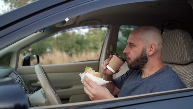 Transportation and vehicle concept. Real man eating food fast food and drink coffee while driving the car during going to work on highway road