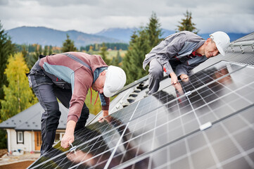 Professional technicians adjusting solar photovoltaic cells. Installation of a solar panel. Two male workers carefully securing battery on a roof.