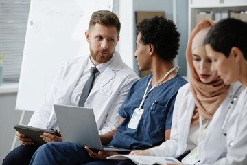 Portrait of two doctors in audience at medical seminar sitting in row and discussing issues