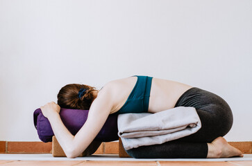 Woman doing restorative yoga child's pose with props - obrazy, fototapety, plakaty