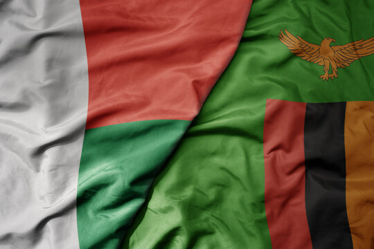 big waving national colorful flag of madagascar and national flag of zambia .