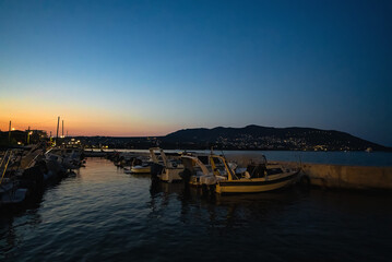Boats in the harbor in the city of Porto Rafti in Greece at sunset.
