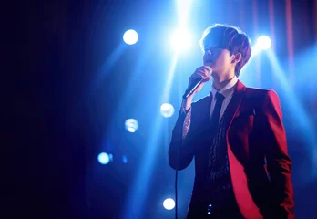 Fotobehang Korean K-pop elegant young male singer boy performing music on live stage while holding microphone in blue spotlight with copy space © J S