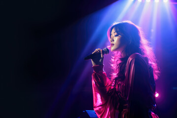 Beautiful Korean K-pop female singer singing romantic ballad music on live stage while holding microphone in retro pink and blue light with copy space - obrazy, fototapety, plakaty