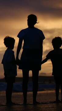 At sunset by the sea, a joyful family, mother, kids, and dad, create silhouettes reaching towards the sun. Kid's dreams come true. Vertical video