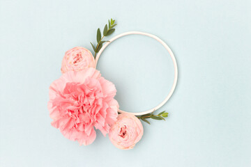 Round frame made of pink rose, carnation flowers and green eucalyptus branches on a blue background. Floral layout.
