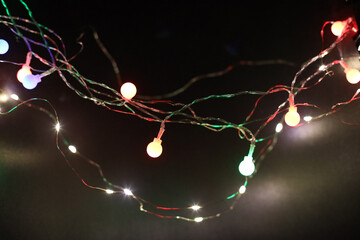 Soft focus smoke blur Christmas color garland lights on dark wall background.