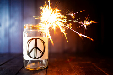 Hope for peace, still life with glass jar with peace symbol and burning sparkler. Background with...