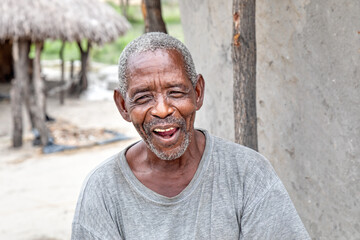 old african village man with a happy face in front of his hut with a thatched roof