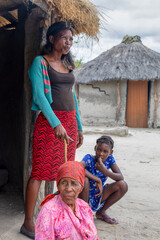 family of three, granny, mother and child, in front of the shack in the sandy back yard in a...