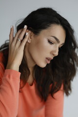 Fototapeta premium Beautiful woman of 30 years old sitting on chair, white background. Portrait of brunette girl smile. Orange sweater and light jeans. Woman barefeet, thoughtful.