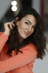 Fototapeta premium Beautiful woman of 30 years old sitting on chair, white background. Portrait of brunette girl smile. Orange sweater and light jeans. Woman barefeet, thoughtful.