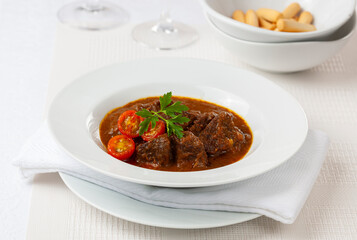 Beef and cherry tomato stew on white plate. Hungarian goulash.