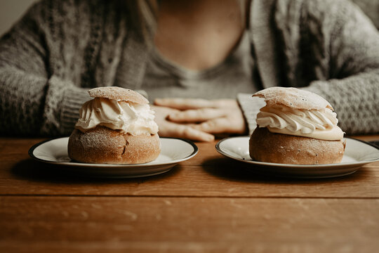 Concept of picking pastry to eat. Focus on traditional Swedish pastry, semla, on the plates at wooden table. In the background, out of focus, a person with hands on table. Photo taken in Sweden.