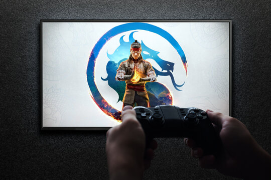 Mortal Kombat 1 game on TV screen with gamepad in hand on black textured wall with light.