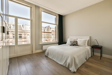 a bedroom with wood flooring and white bedding in front of large windows looking out onto the city skyline