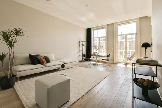 a living room with wood flooring and white furniture in the photo is taken to the right, there are some plants on the