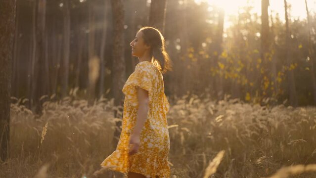 beautiful happy woman in white light dress jogging, spinning joyfully in fall forest between golden spikelets of tall dry grass. romantic girl relaxing in magic autumn forest with wonderful sunlight