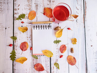 Notebook, tea cup and autumn leaves on wooden background