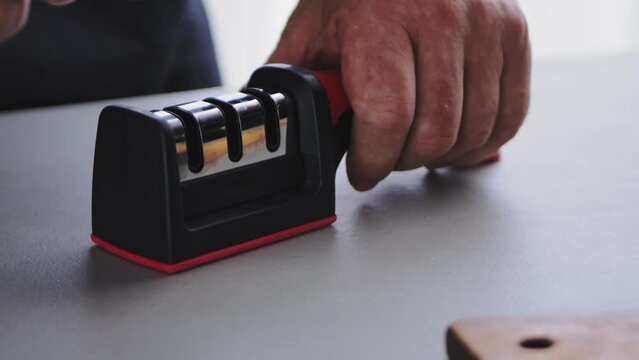 A woman's hand sharpens a kitchen knife in a special knife sharpener on the table. Slow motion