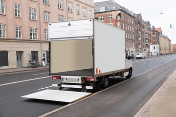 Empty white delivery truck with tailgate open parked in the street with shops and buildings. Copy space. - 679373436