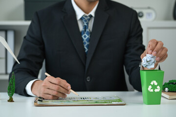Businessman put paper waste on small tiny recycle bin in his office symbolize corporate effort on...