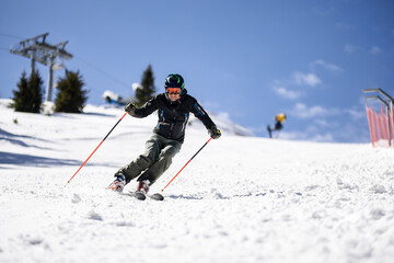Professional skier skiing on slopes in a mountain winter resort. Sunny day with clear sky.