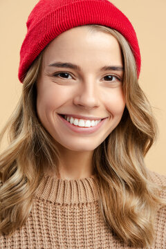 Closeup portrait smiling attractive woman wearing red hipster hat and stylish winter sweater looking at camera isolated on beige background. Positive lifestyle, natural beauty concept 