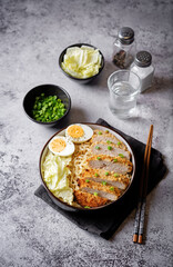 Ramen noodles with meat schnitzel slices, peking cabbage, eggs and scallions in a bowl