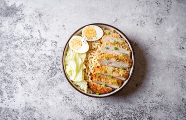 Ramen noodles with meat schnitzel slices, peking cabbage, eggs and scallions in a bowl